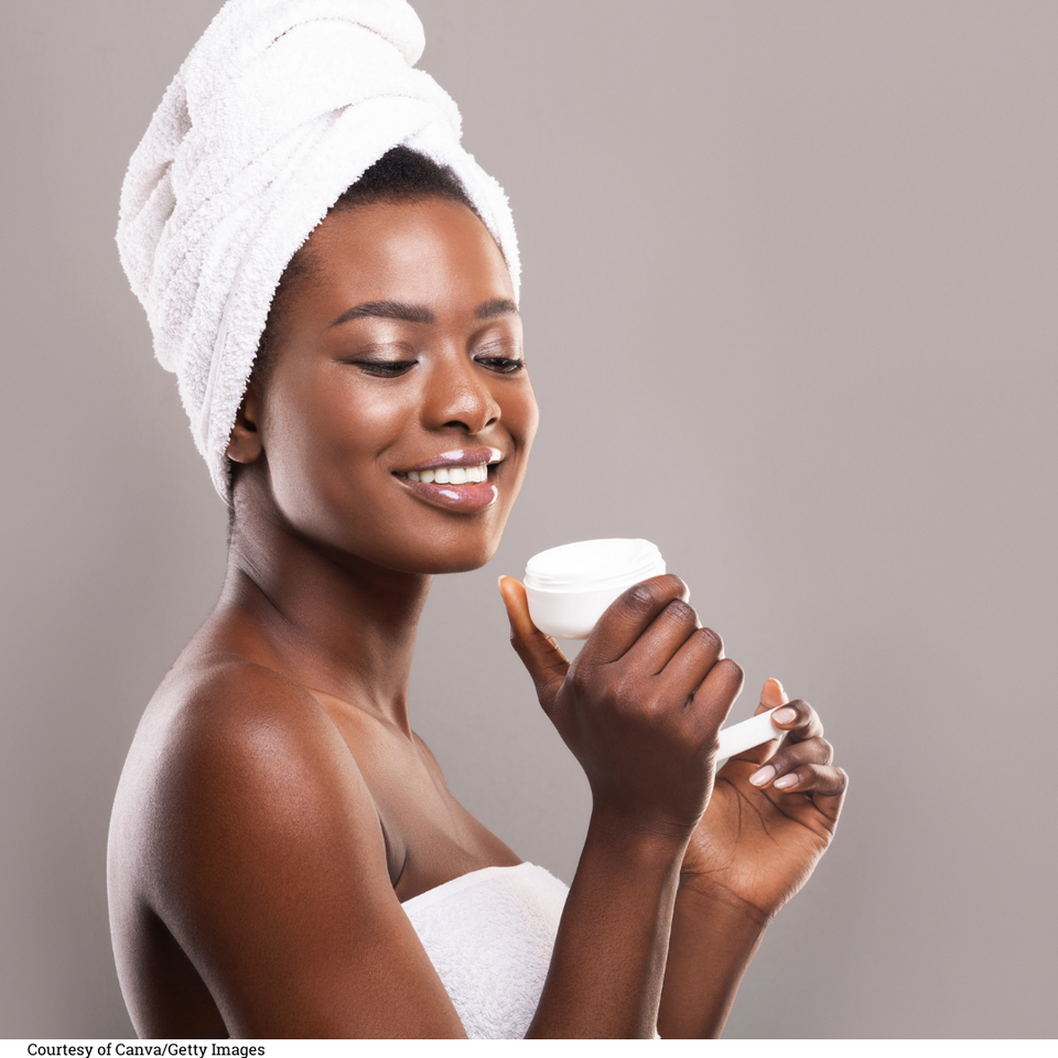 Skincare is Healthcare. Black woman with hair wrapped in a towel smiling while looking at a jar of moisturizer